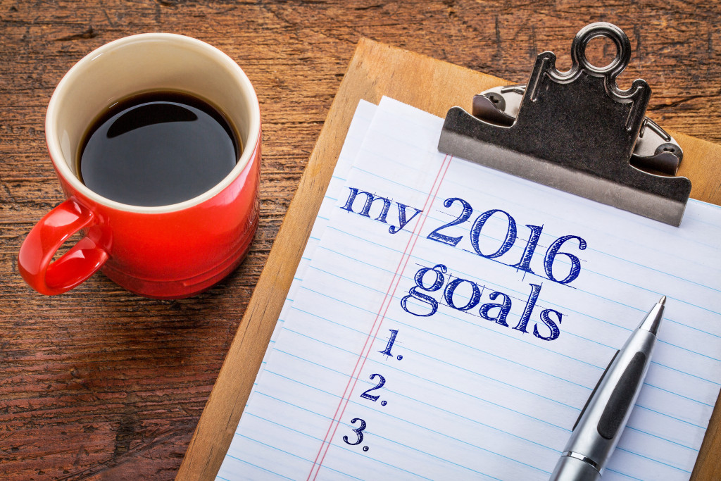 my 2016 goals list on clipboard and coffee against grunge wood desk